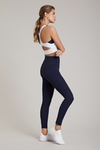 Full body length side view of a woman in a white crop top and navy leggings
