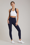 Full body length front view of a woman in a white crop top and navy leggings