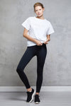 Full body length front view of a woman wearing Silou Tee - White and black leggings with hands at the waist