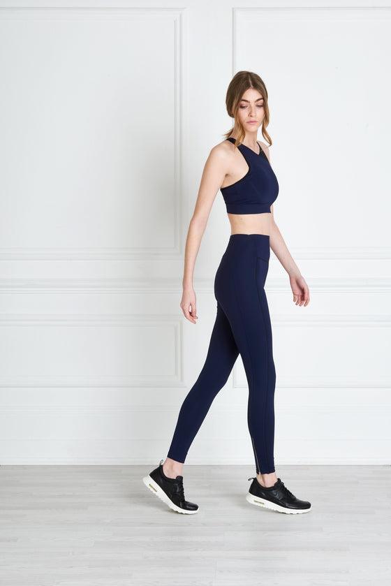 Full body length side view of a woman wearing Bridget Sports Bra - Navy and navy leggings