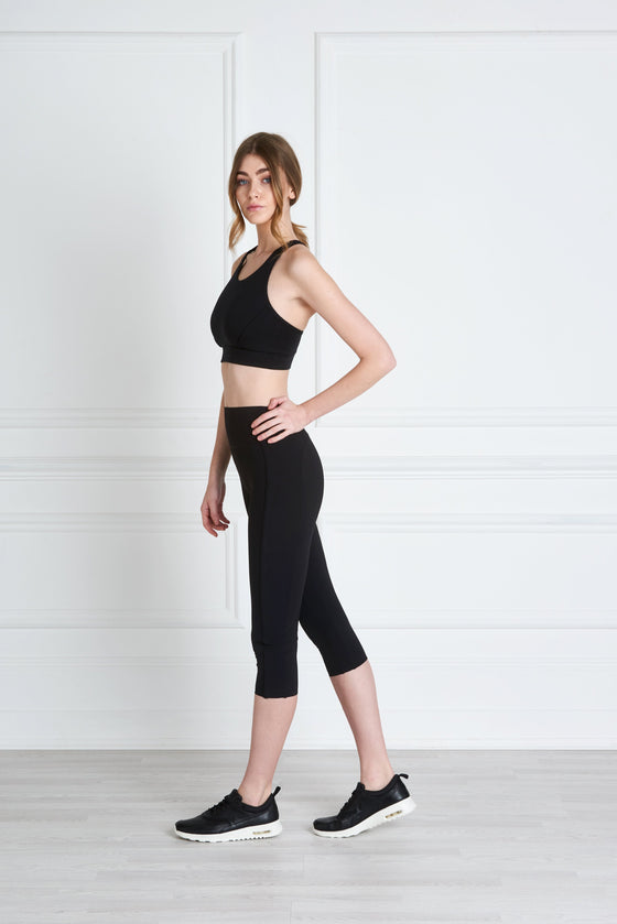 Full body length side view of a woman wearing Nadya Crop Legging - Black and a black crop top