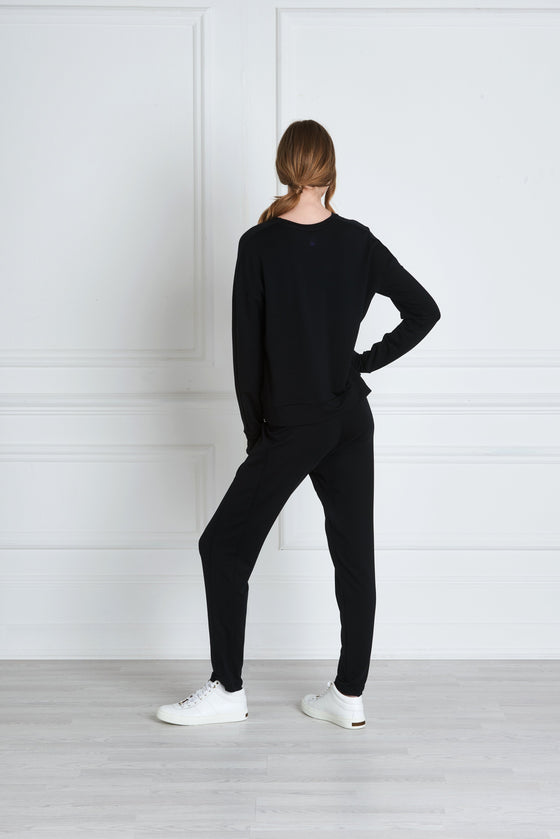 Full body length back view of a woman wearing Uma Sweatpant - Black and a black sweatshirt